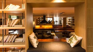 A modern library with bookshelves, a seating area with cushions, and a staircase leading to another level. - Wangshan Travelling With Hotel (Lijiang)