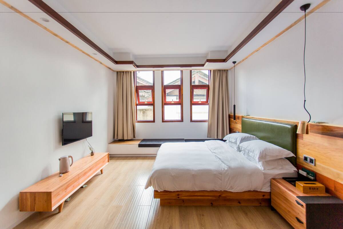 Un dormitorio moderno con una cama de madera, un televisor montado en la pared y un ventanal con cortinas.
