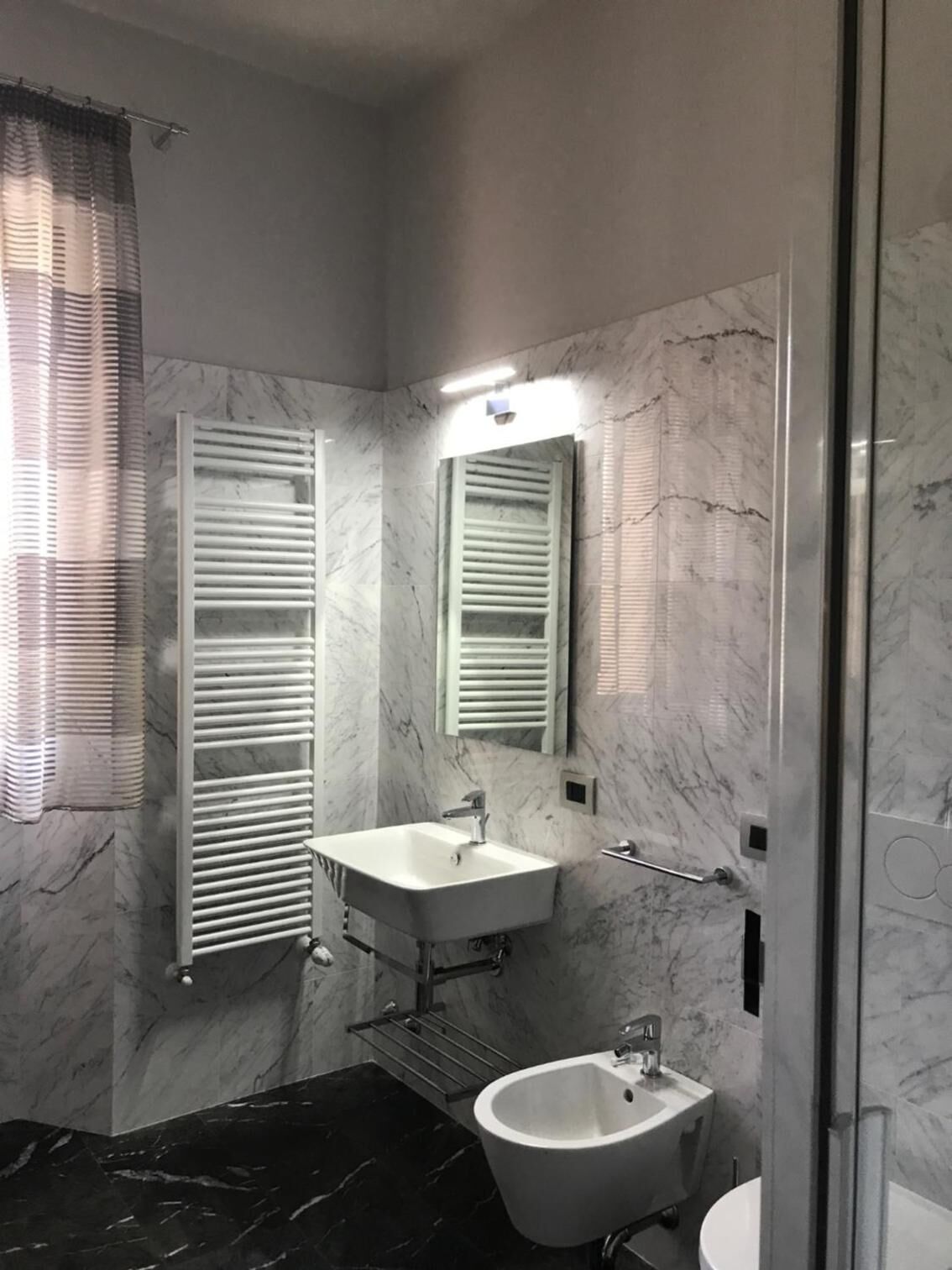 A modern bathroom with a marble floor, a white sink, a bidet, and a glass-enclosed shower.