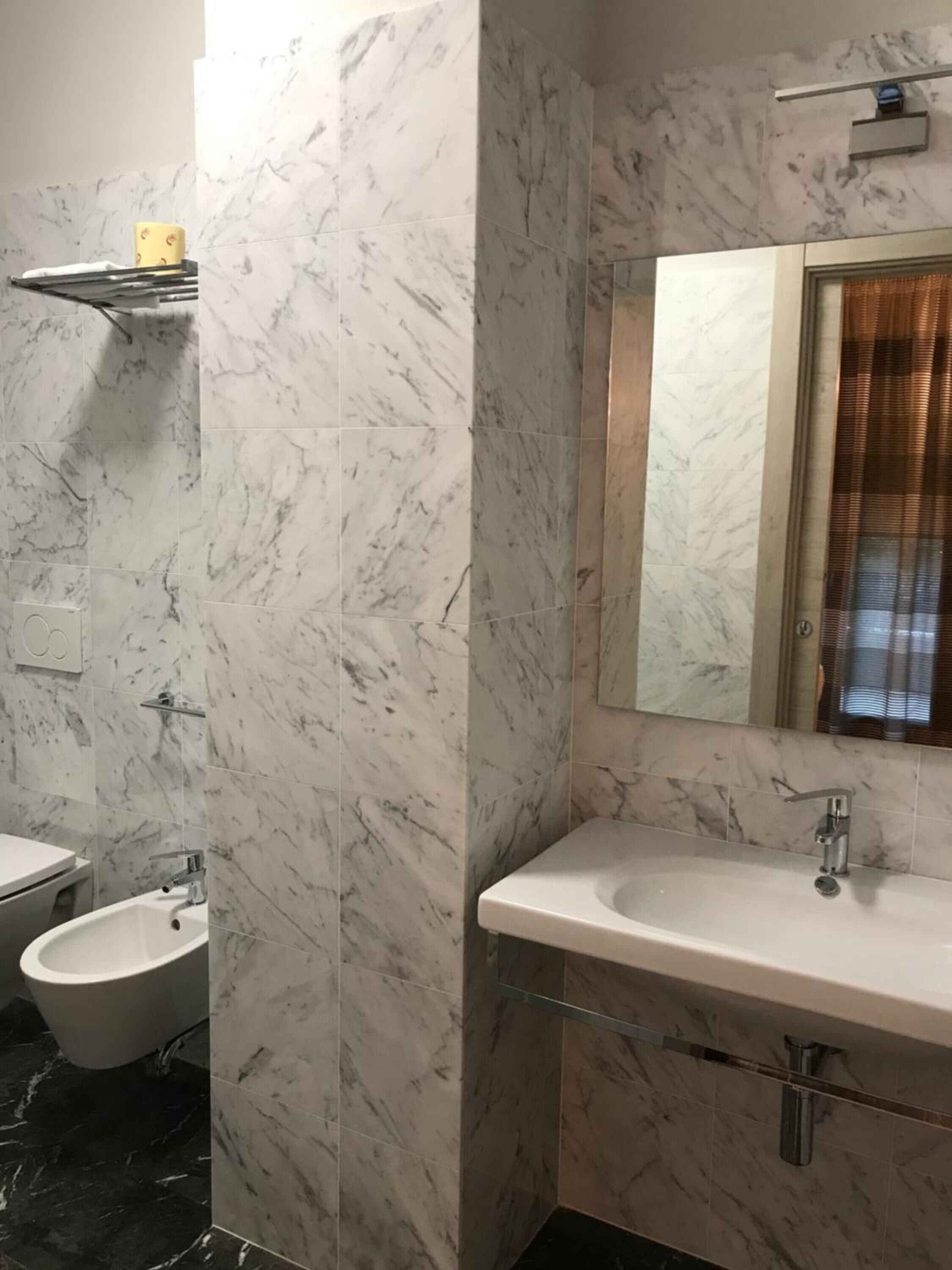 Un bagno con parete in marmo, lavabo, water e specchio.