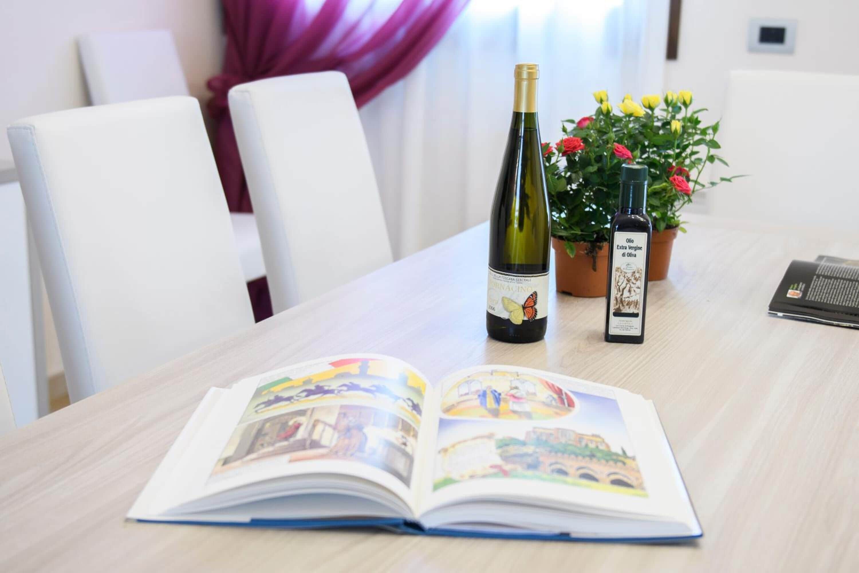 Een tafel met een open boek, een fles wijn en een fles olijfolie.