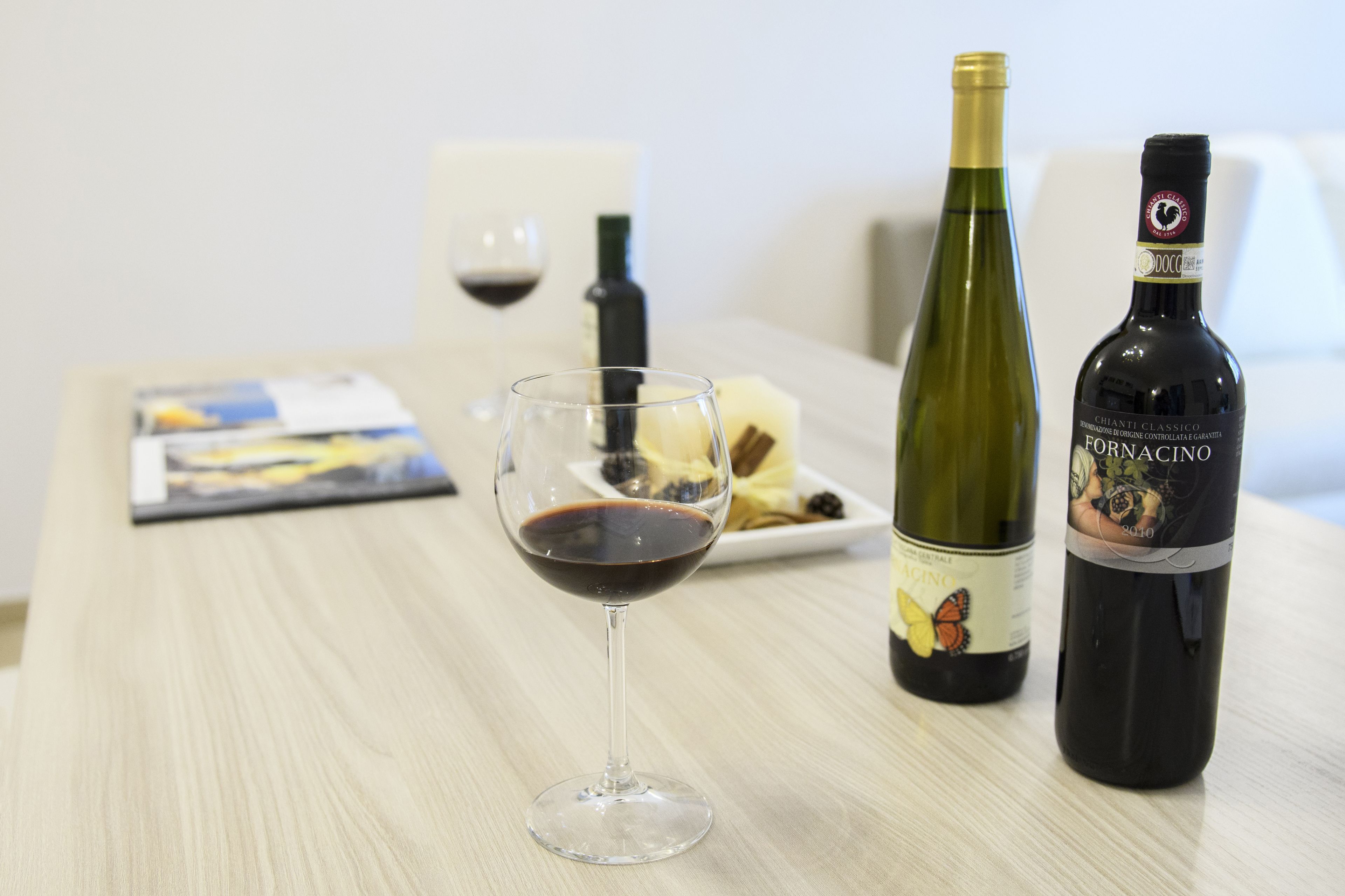 A table with a wine glass, two wine bottles, a candle, and a plate with food.