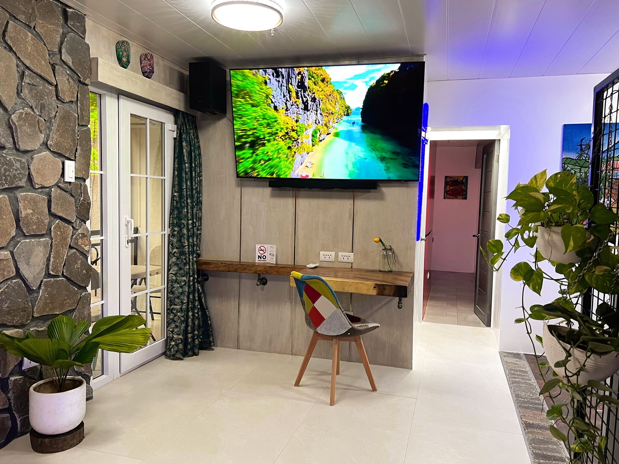 A living room with a stone wall, a TV mounted above a wooden bar, a chair, and a potted plant.