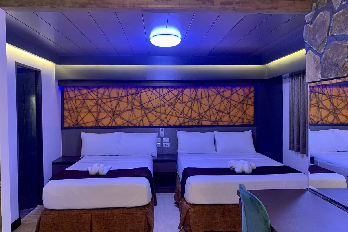 Habitación de hotel con dos camas, un muro de acento de piedra, una lámpara de techo moderna y un escritorio pequeño.