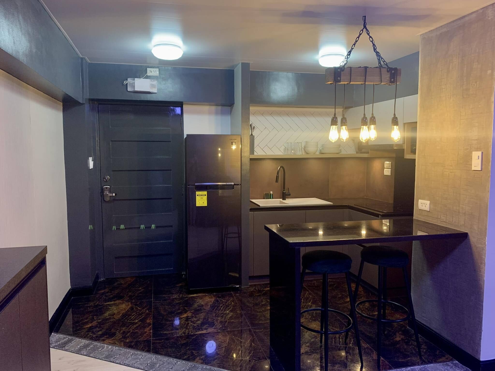 A compact kitchen with a black refrigerator, a sink, and a bar area with stools.