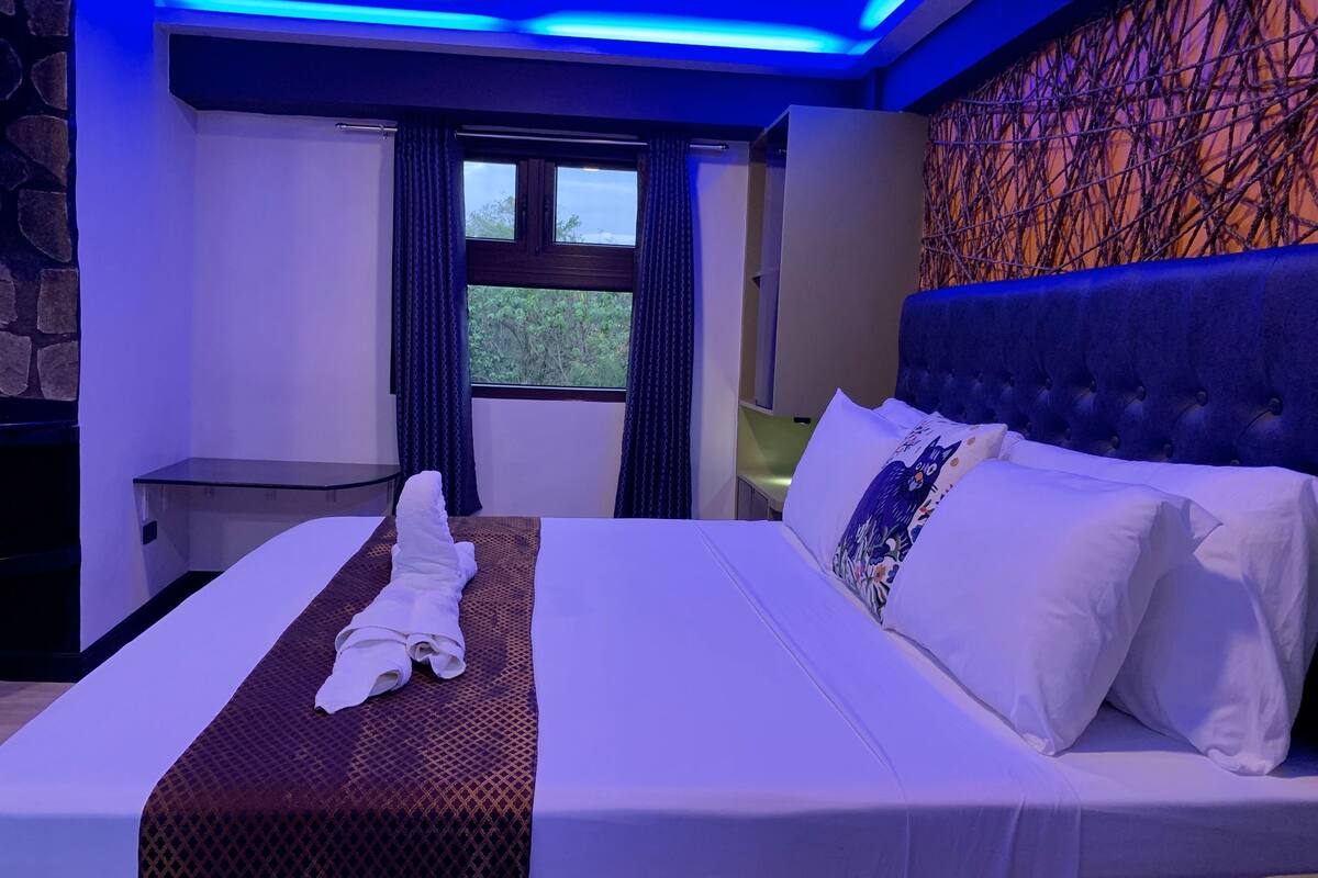 Habitación de hotel moderna con una cama bien hecha, vistas por la ventana y un detalle de pared de piedra.