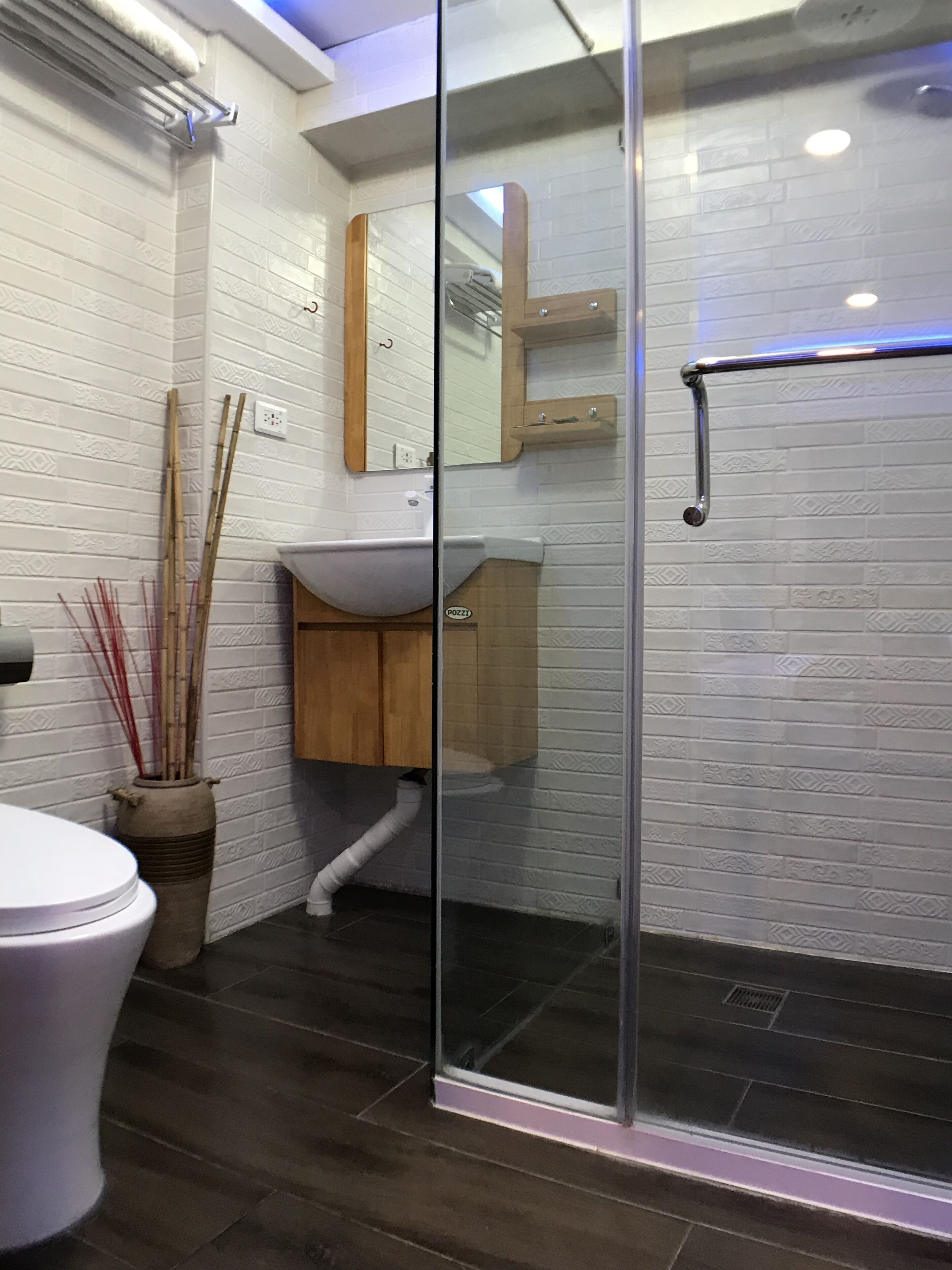 A modern bathroom with a glass shower enclosure, white subway tile walls, a wooden vanity, and a white toilet.