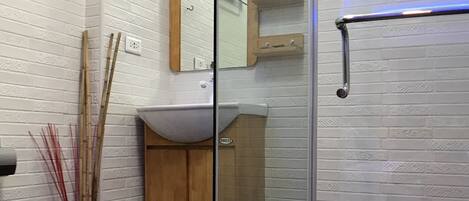 Un baño moderno con cabina de ducha de vidrio, paredes de azulejos tipo metro blancos, tocador de madera y inodoro blanco.