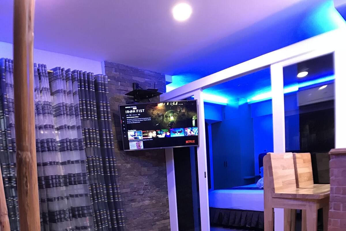 Una sala de estar moderna con un televisor de pantalla plana montado en la pared, una silla de madera y un sofá.