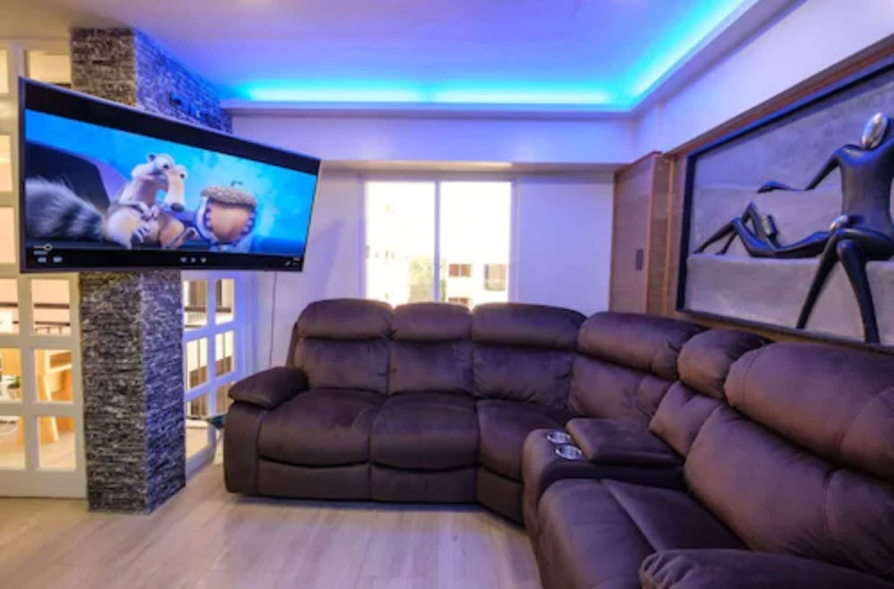 A modern living room with a large flat-screen TV, a brown leather sofa, and a stone accent wall.