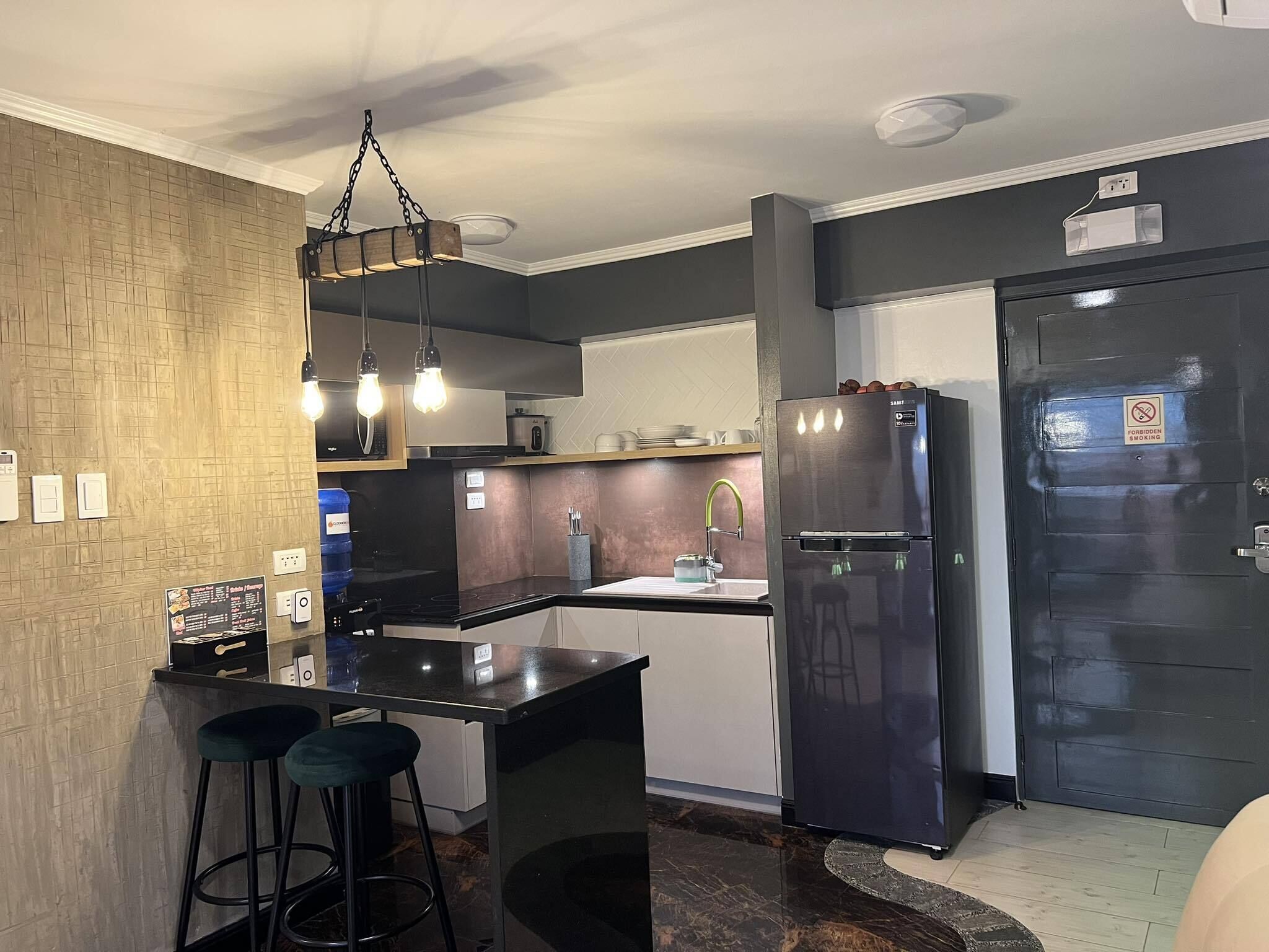 A modern kitchen with a black countertop, stainless steel appliances, and a bar stool.