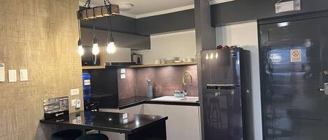 A modern kitchen with a black countertop, stainless steel appliances, and a bar stool.