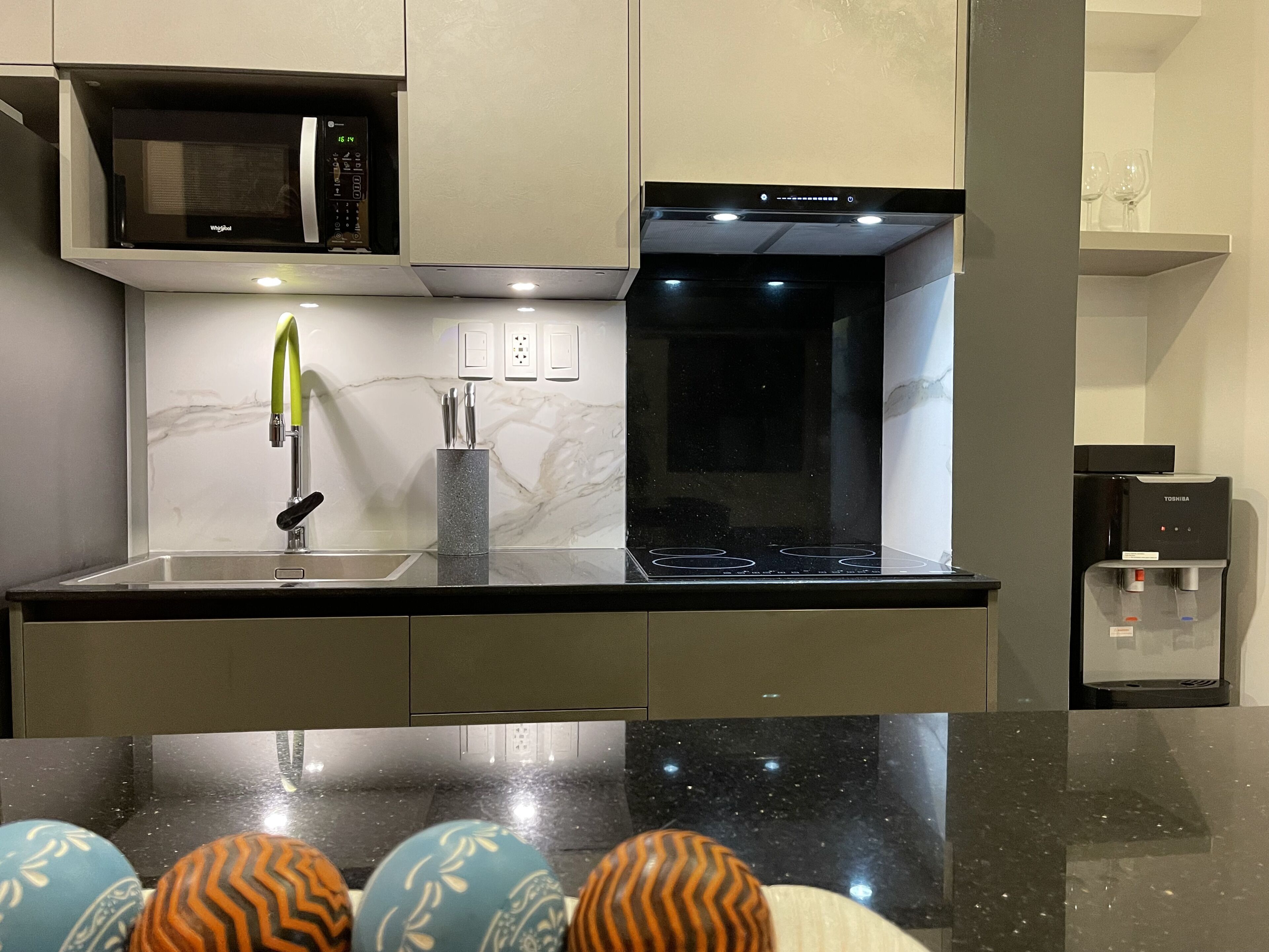 A modern kitchen with a black countertop, a built-in microwave, a stove, and a water dispenser.
