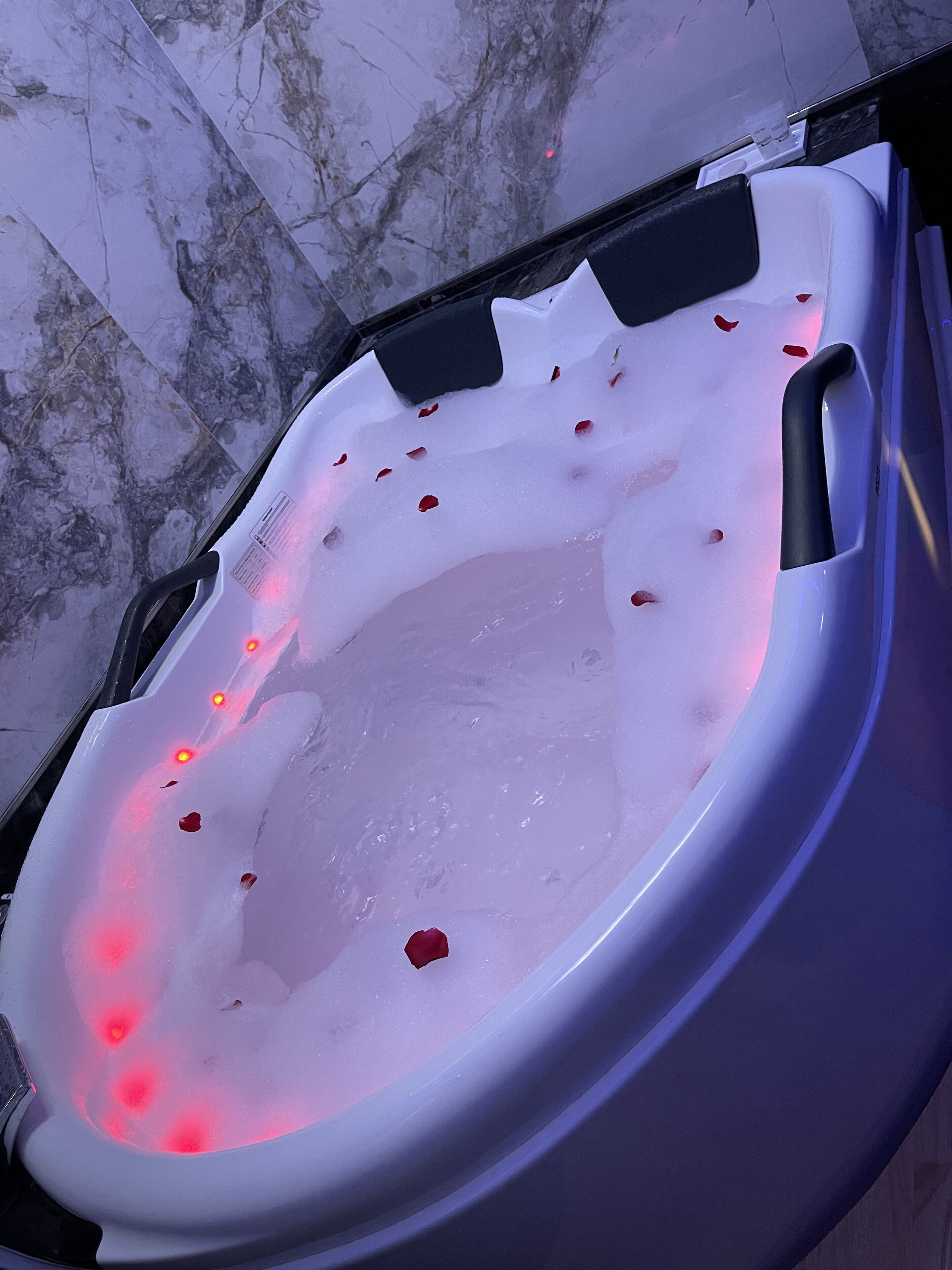 A hot tub with water, rose petals, and red lights.