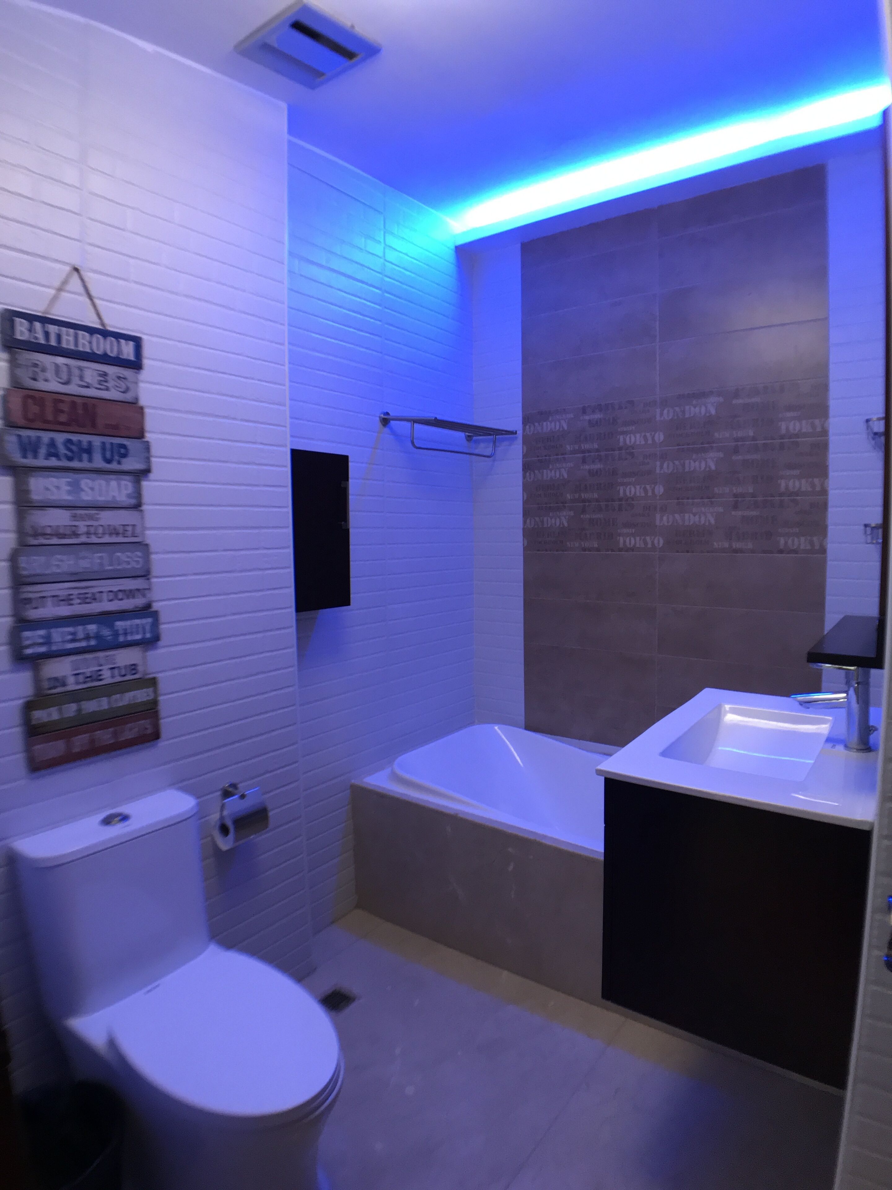 A bathroom with a toilet, a sink, and a bathtub. There is a sign on the wall listing bathroom rules.
