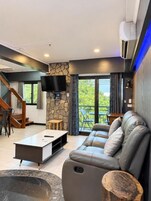 Una sala de estar moderna con sofá, mesa de centro y televisor. Una escalera conduce a otro nivel.