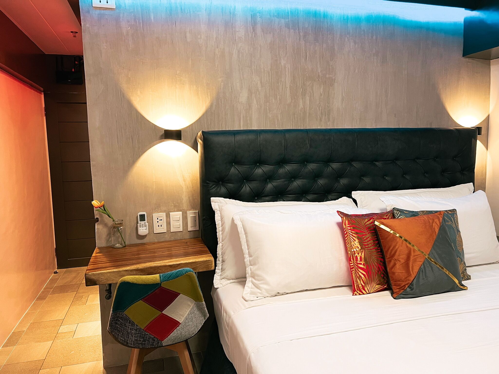 A hotel room with a bed, a bedside table, a chair, and two wall-mounted lamps.