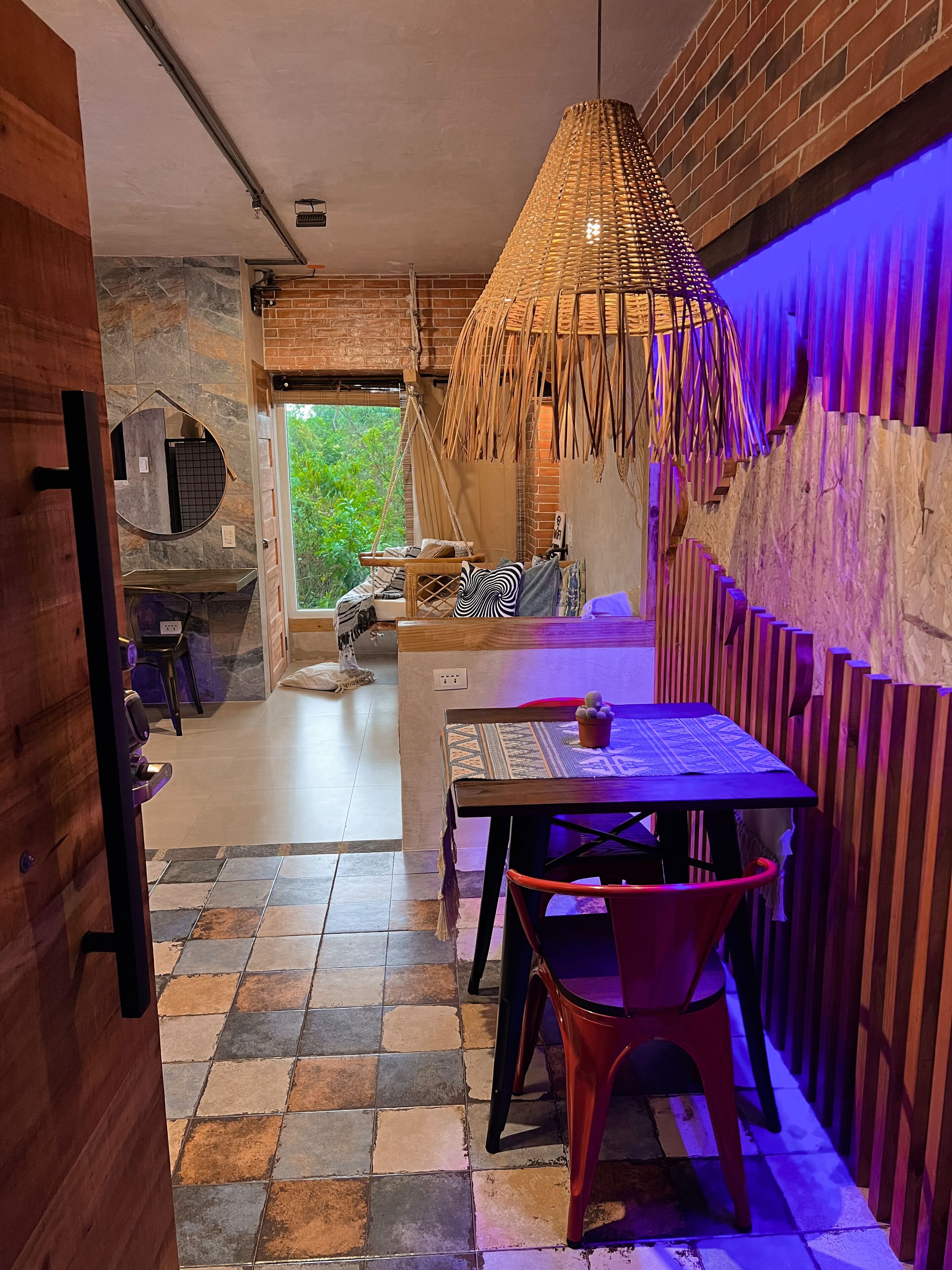 Un interior moderno con comedor, que incluye una mesa, sillas, lámpara colgante y vistas al exterior.