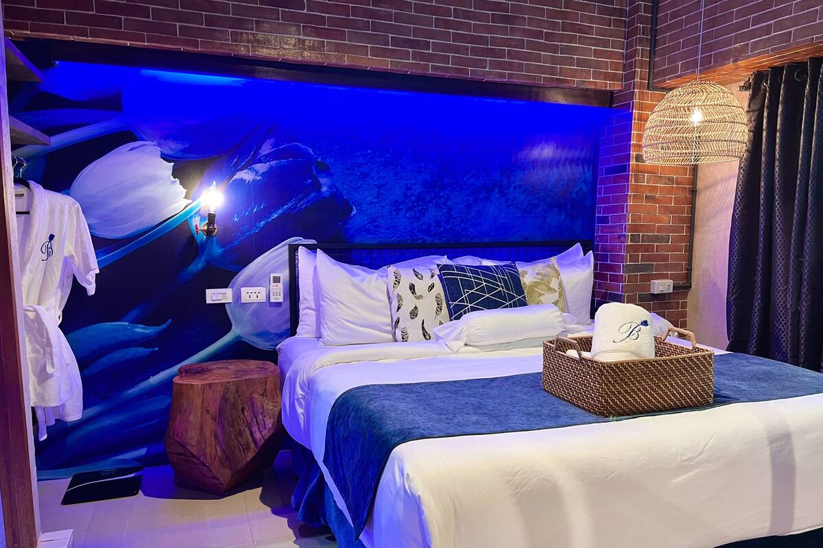 Una habitación de hotel con una cama, una mesita de noche, un teléfono en la pared y una pared con un mural azul.