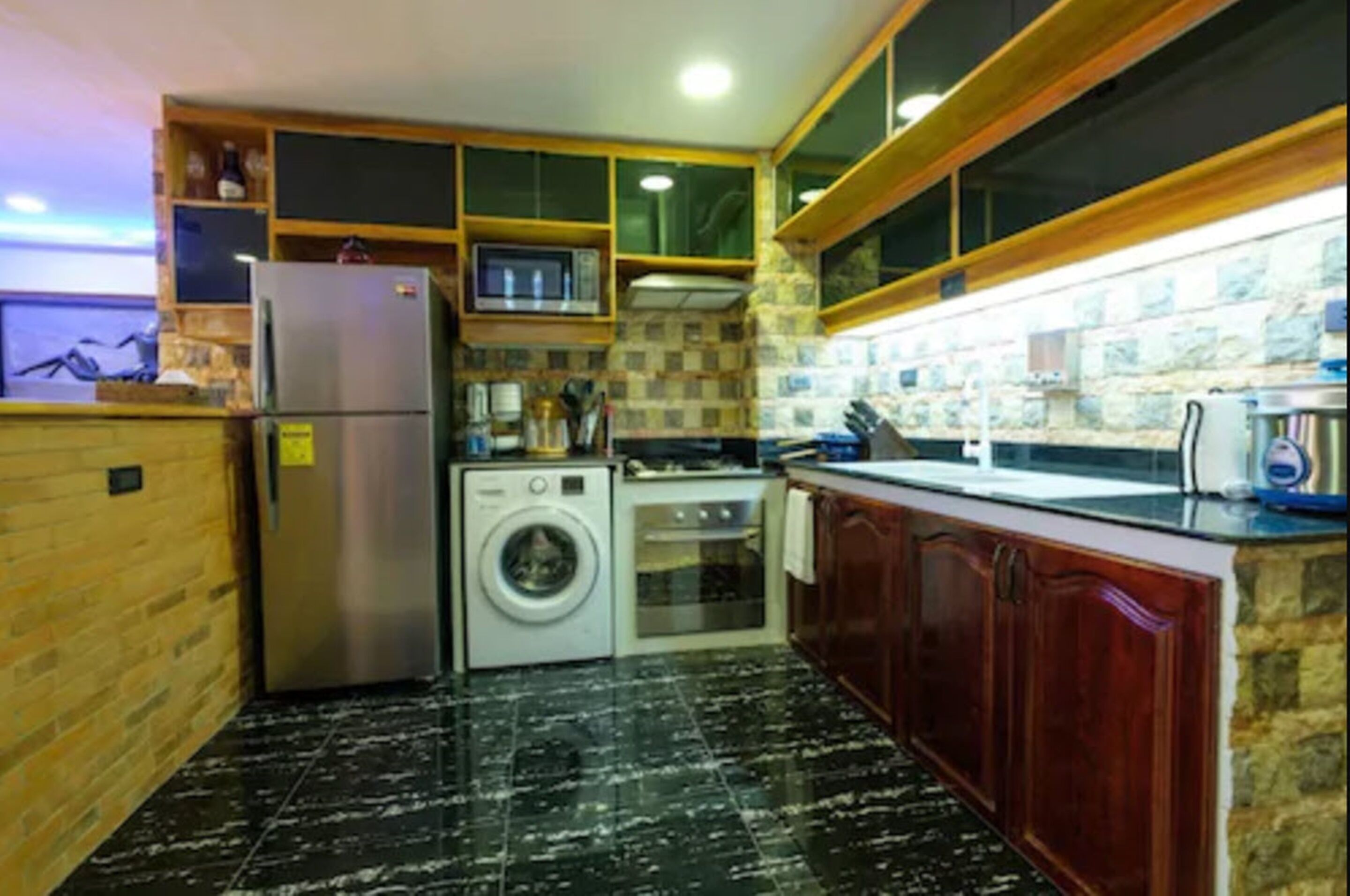 A compact kitchen with a refrigerator, washing machine, oven, and wooden cabinets.