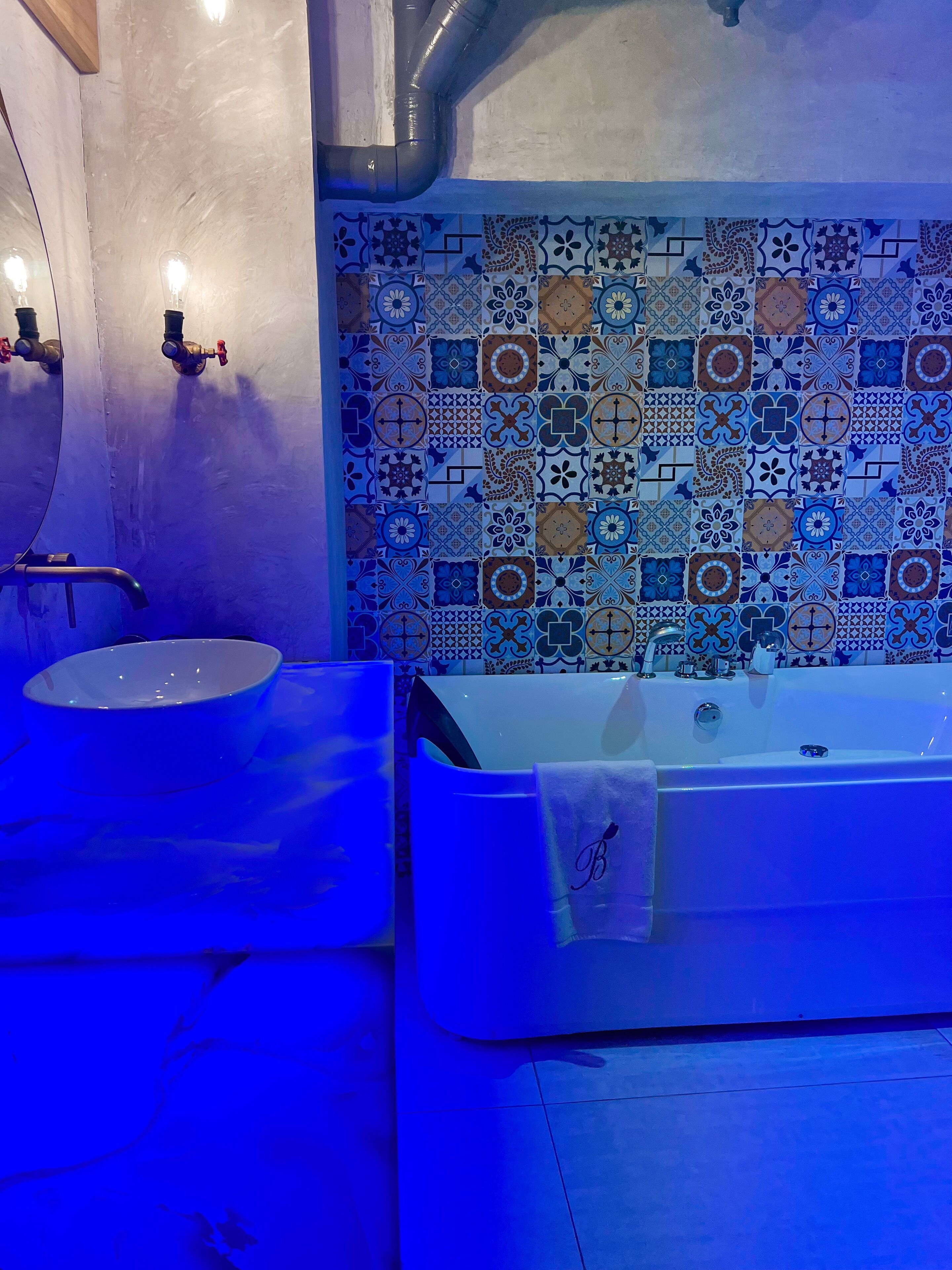 A bathroom with a white sink, a bathtub, and a tiled wall with a variety of patterns.