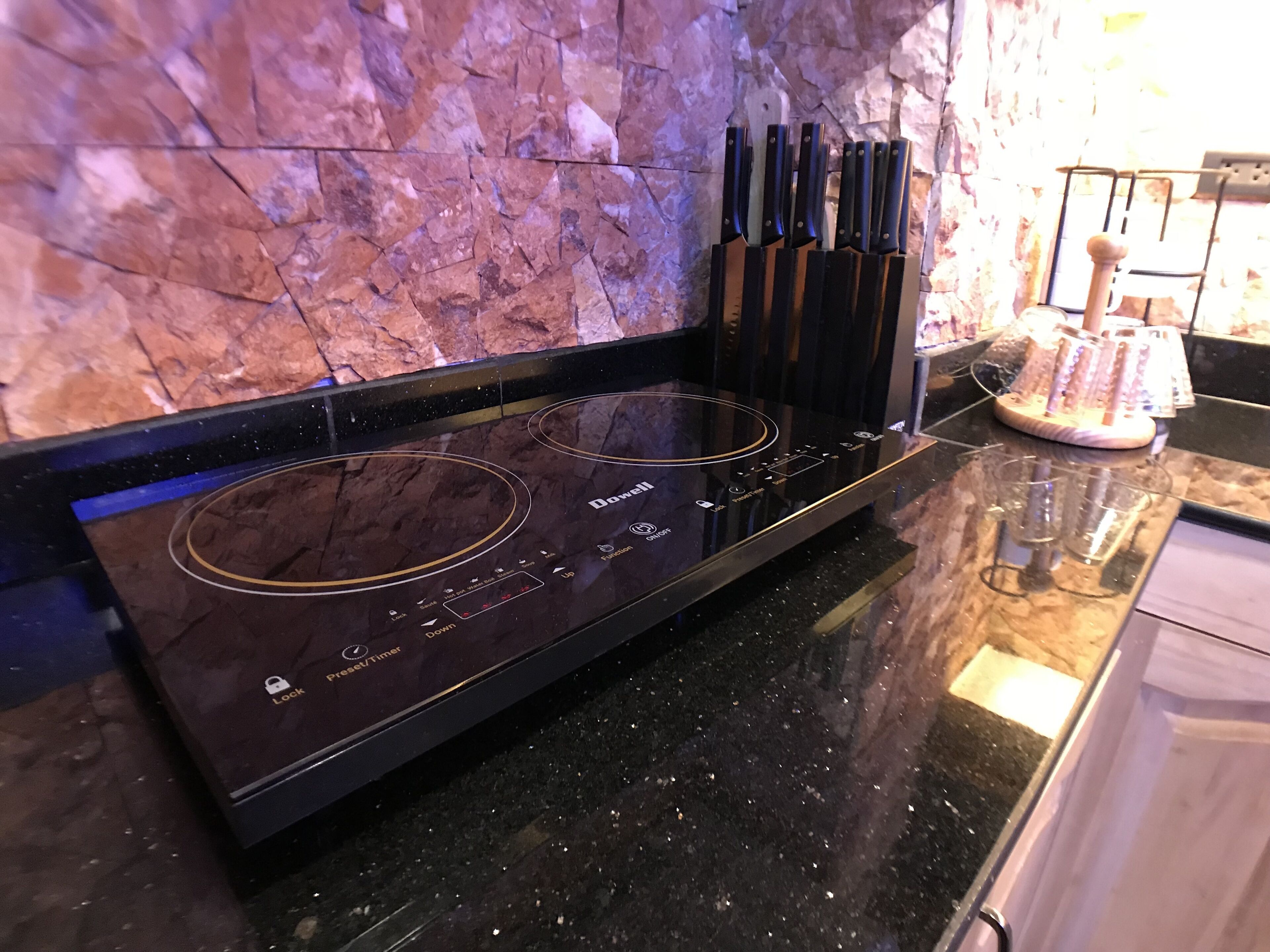 Une cuisine moderne dotée d’une plaque de cuisson à induction noire, d’un pare-feu en pierre et d’un bloc à couteaux posé sur le plan de travail.