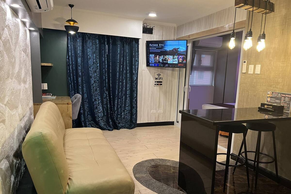 Una sala de estar moderna con un sofá, televisor y una zona de cocina con barra.