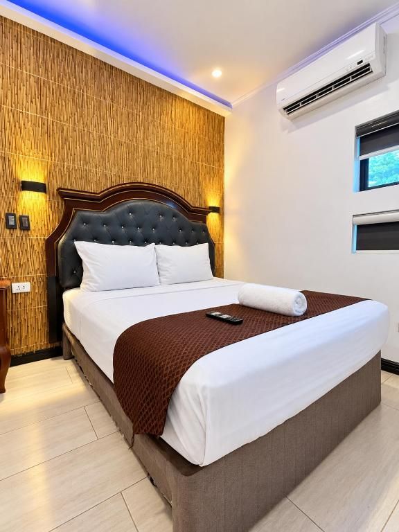 A hotel room with a large bed, a wooden accent wall, and an air conditioning unit.