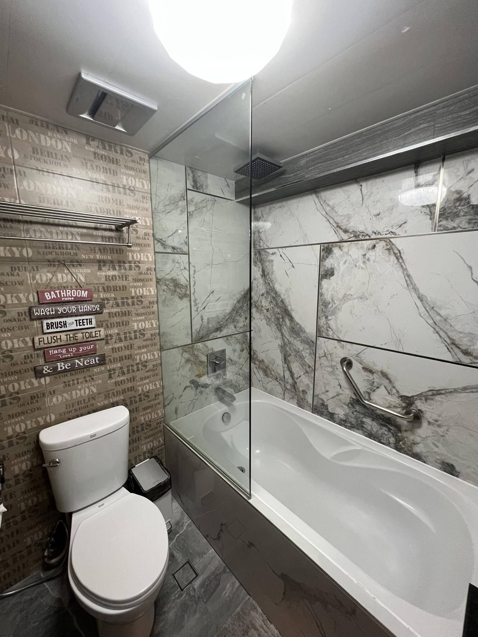 Un baño moderno con inodoro, ducha envuelta en vidrio y pared de azulejos de mármol con indicaciones.