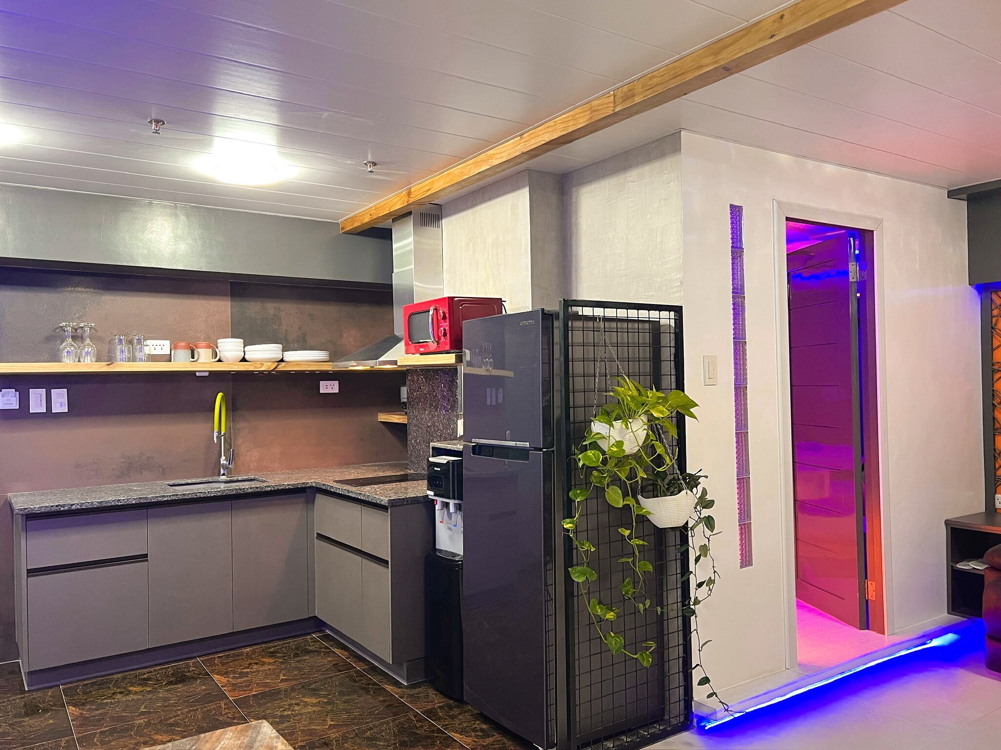 A modern kitchen with grey cabinets, a black refrigerator, and a microwave on a wooden shelf.