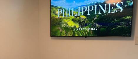 A hotel room with a bed, a wall-mounted TV displaying 'PHILIPPINES LIFESTYLE HAL', and a towel art on the bed.