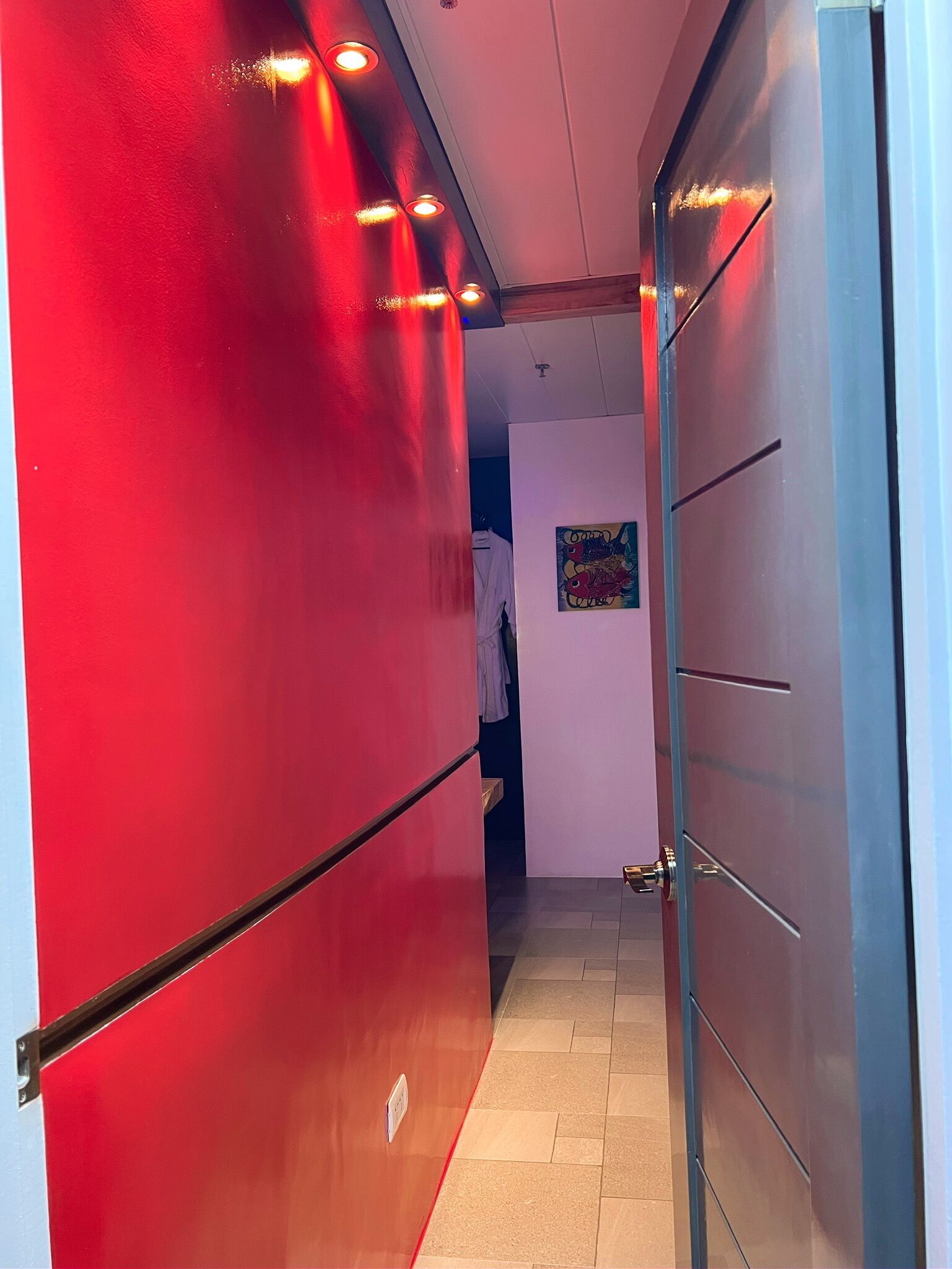 Un couloir aux murs rouges et une porte donnant sur une pièce.