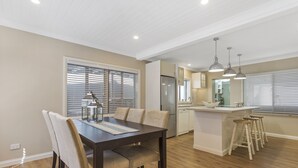 A modern kitchen with a central island, wooden flooring, and pendant lighting. - Hamptons at The Bay (Deception Bay)