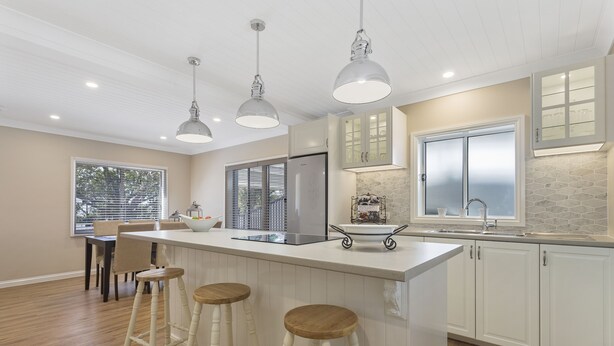 A modern kitchen with a large island, pendant lights, and a view of the outdoors. - Hamptons at The Bay (Deception Bay)