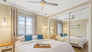 A hotel room with a large bed, a bedside table, a mirror, and a ceiling fan. - Hamptons at The Bay (Deception Bay)