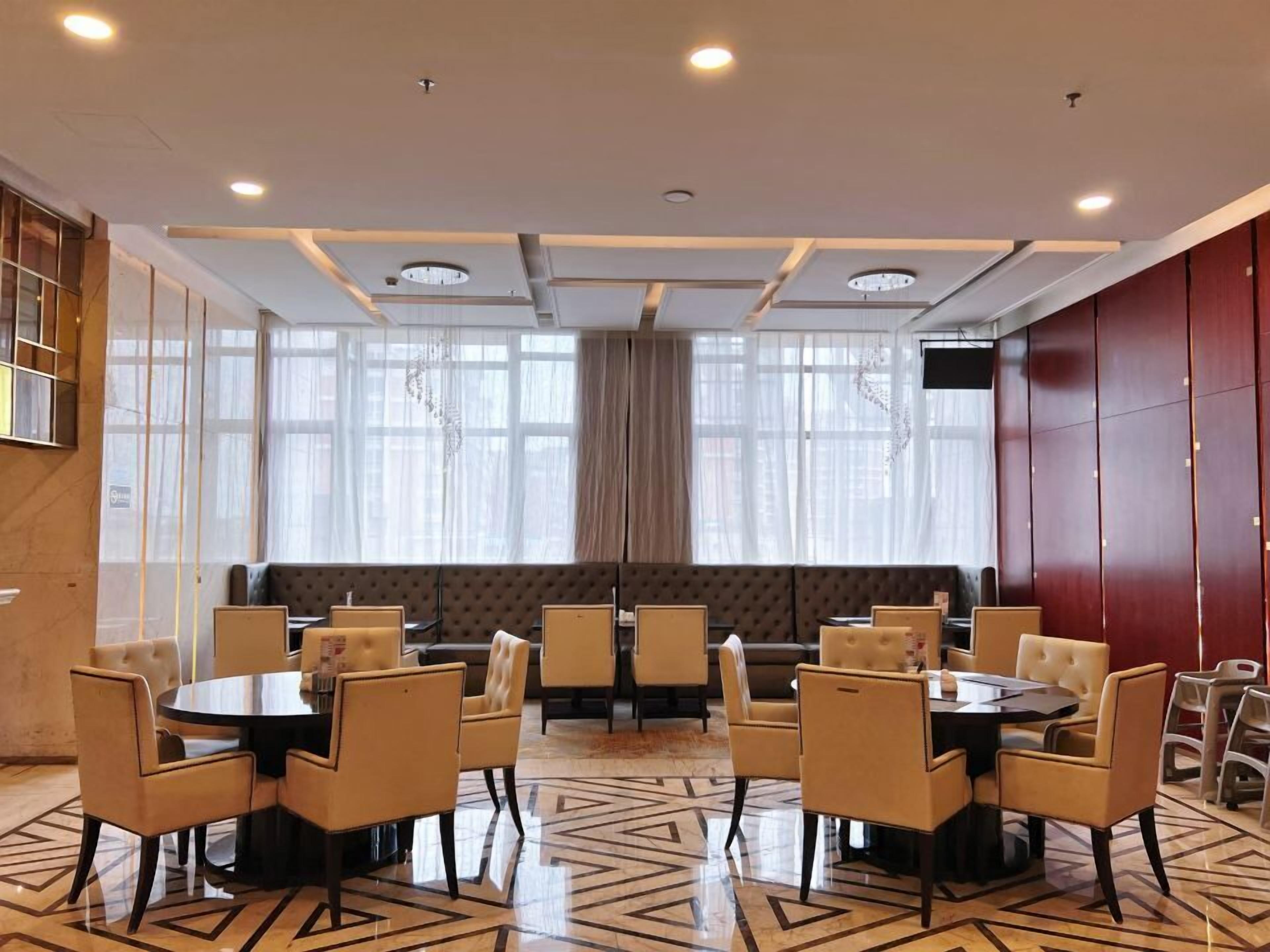 A hotel room with a large bed, a seating area with sofas, a dining table with chairs, and a TV mounted on the wall.