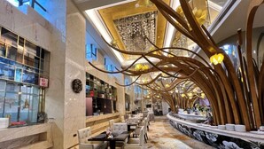 A modern hotel lobby with marble walls, a central seating area with tables and chairs, and a decorative ceiling with wooden elements. - Menshine Gloria Plaza Hotel Shantou (Shantou)