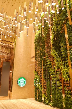 Un interior moderno con el logotipo de Starbucks, vegetación vertical y luces colgantes.