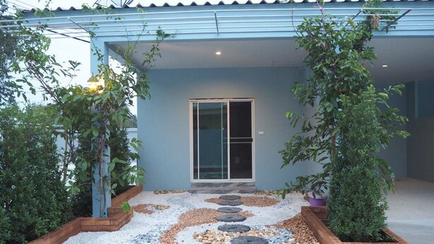 A house with a blue exterior, a glass door entrance, and a garden with stepping stones and plants. - Tai Baan Resort (Phanom Sarakham)