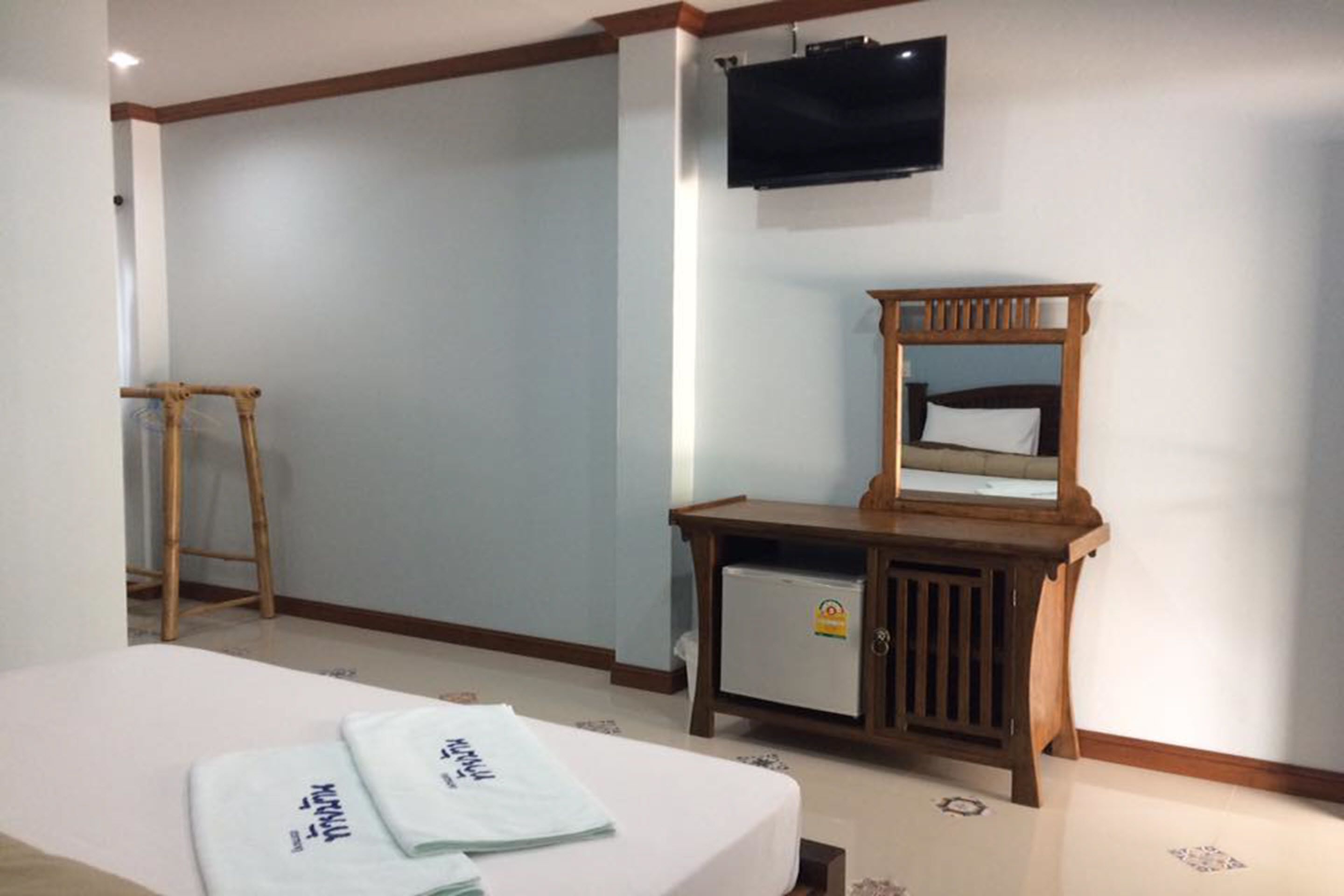 Habitación de hotel con cama, mesita de noche de madera, televisor y un refrigerador pequeño.