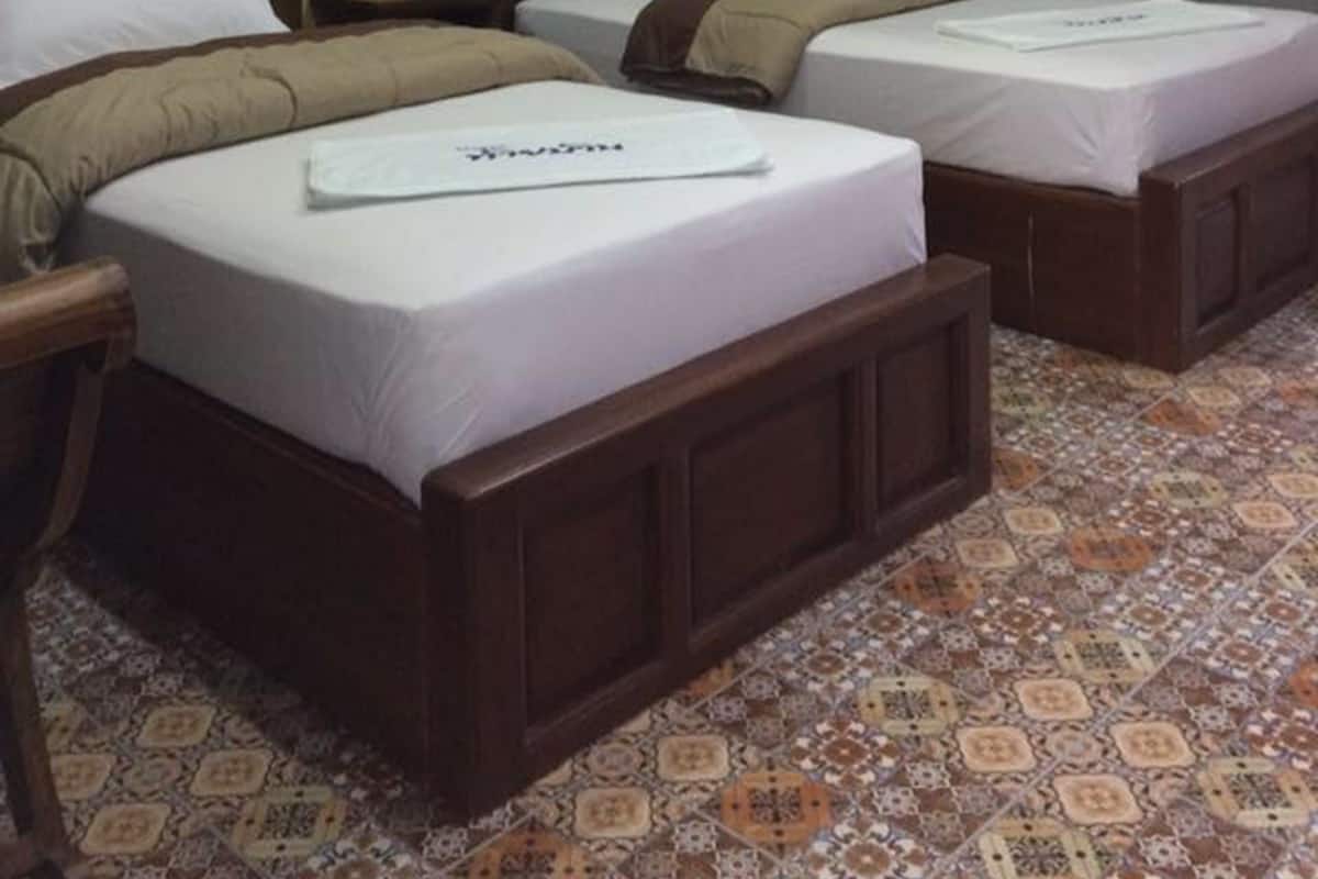A hotel room with two single beds, a wooden headboard, a small bedside table, and a wall-mounted air conditioner.