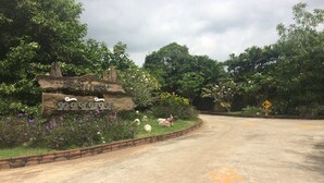 A rural road with a wooden signpost and a brick wall. - Tai Baan Resort (Phanom Sarakham)