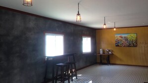 A room with a patterned floor, two windows, a table with chairs, a painting on the wall, and hanging lights. - Tai Baan Resort (Phanom Sarakham)