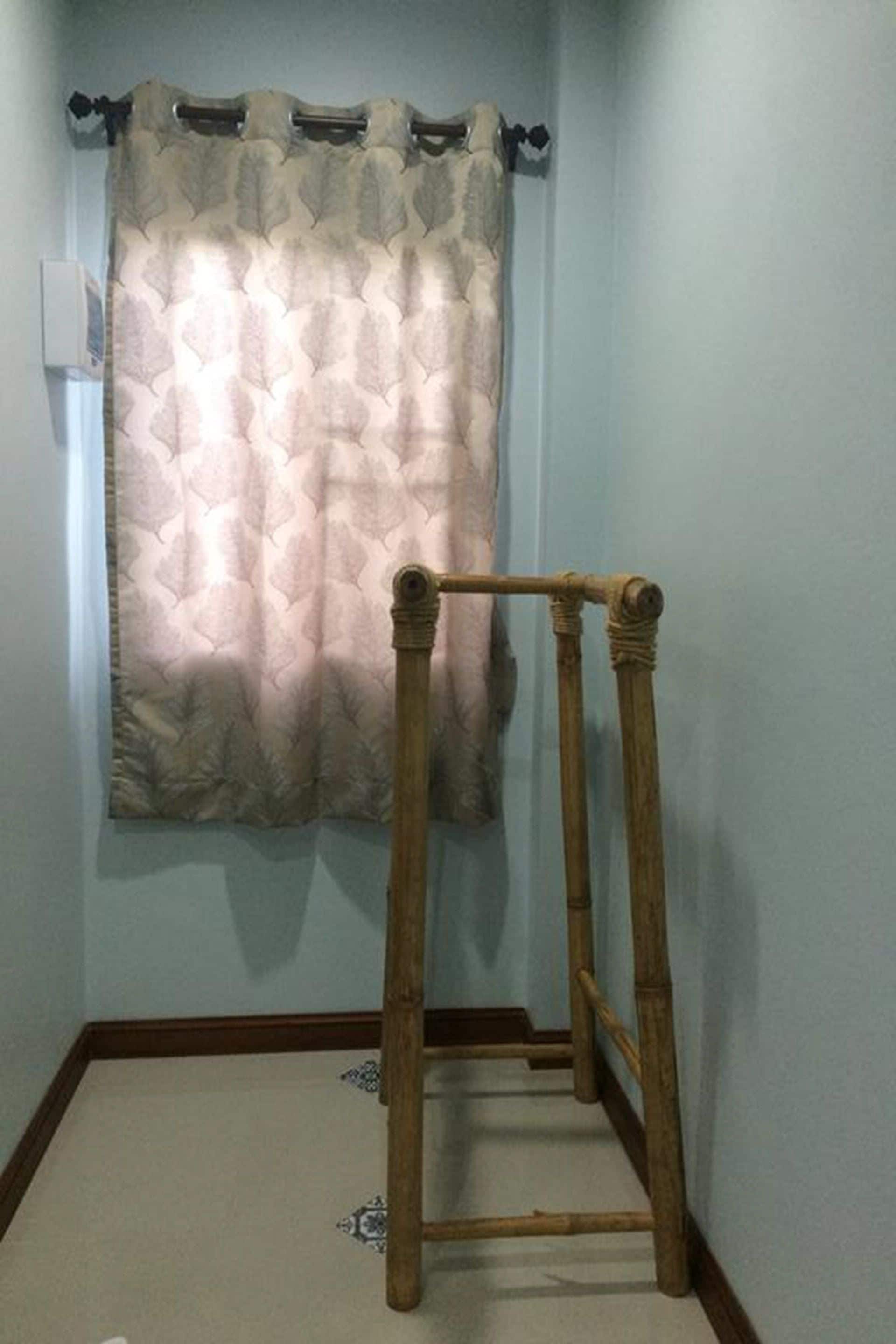 A bathroom with a bamboo stool, a patterned shower curtain, and a light blue wall.