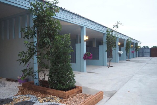 A building with a covered patio area, potted plants, and a gravel pathway. - Tai Baan Resort (Phanom Sarakham)