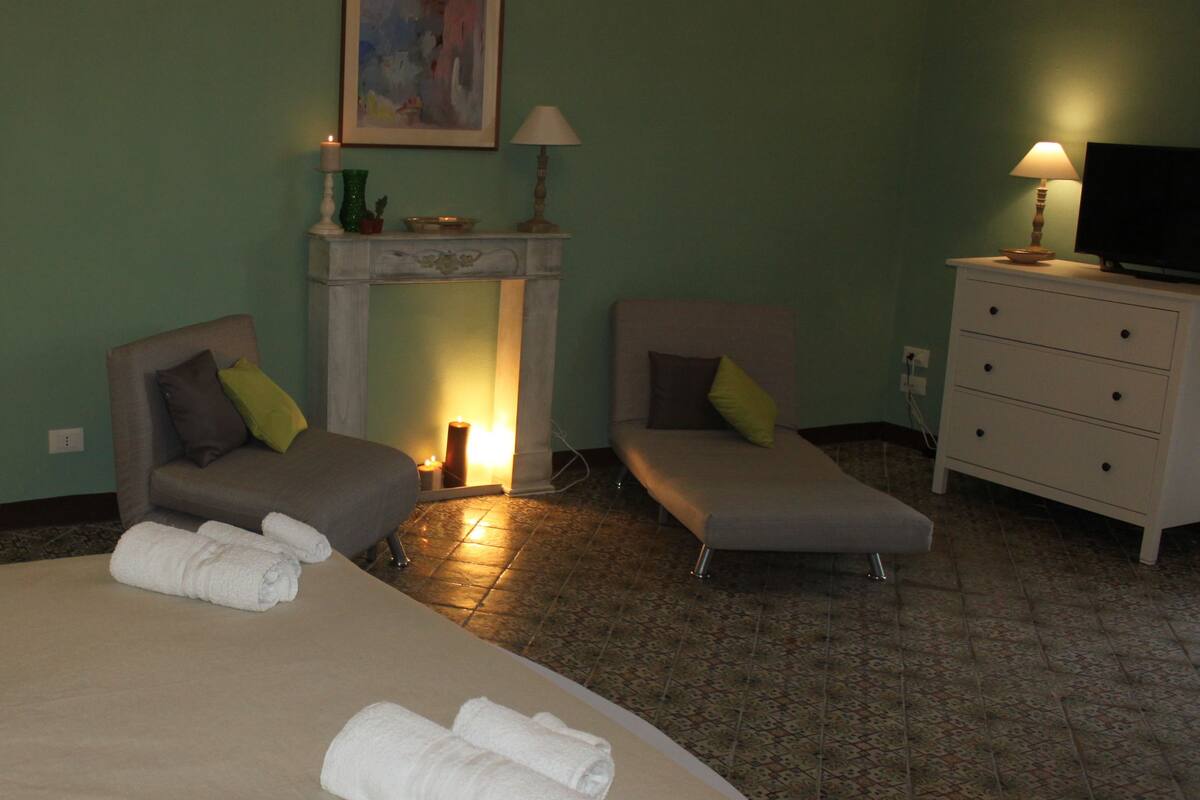 A hotel room with a large bed, two armchairs, a fireplace, a television, and a dresser.