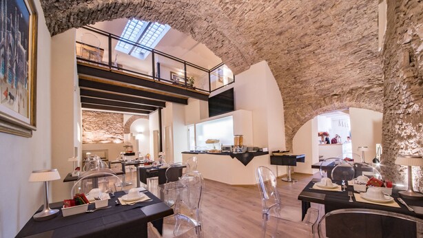 Un espace repas moderne avec des chaises transparentes, des tables noires et un plafond haut laissant apparaître la pierre brute.