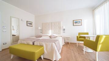 A hotel room with a bed, a small table, two chairs, a bench, and a mirror.