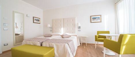 Una habitación de hotel con cama, una mesita, dos sillas, un banco y un espejo.