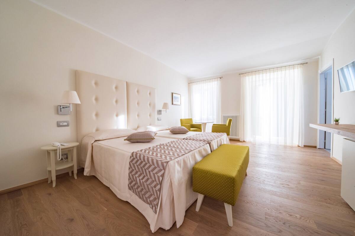 Un dormitorio con una cama grande, mesitas de noche, un banco, una silla y vista de la habitación.